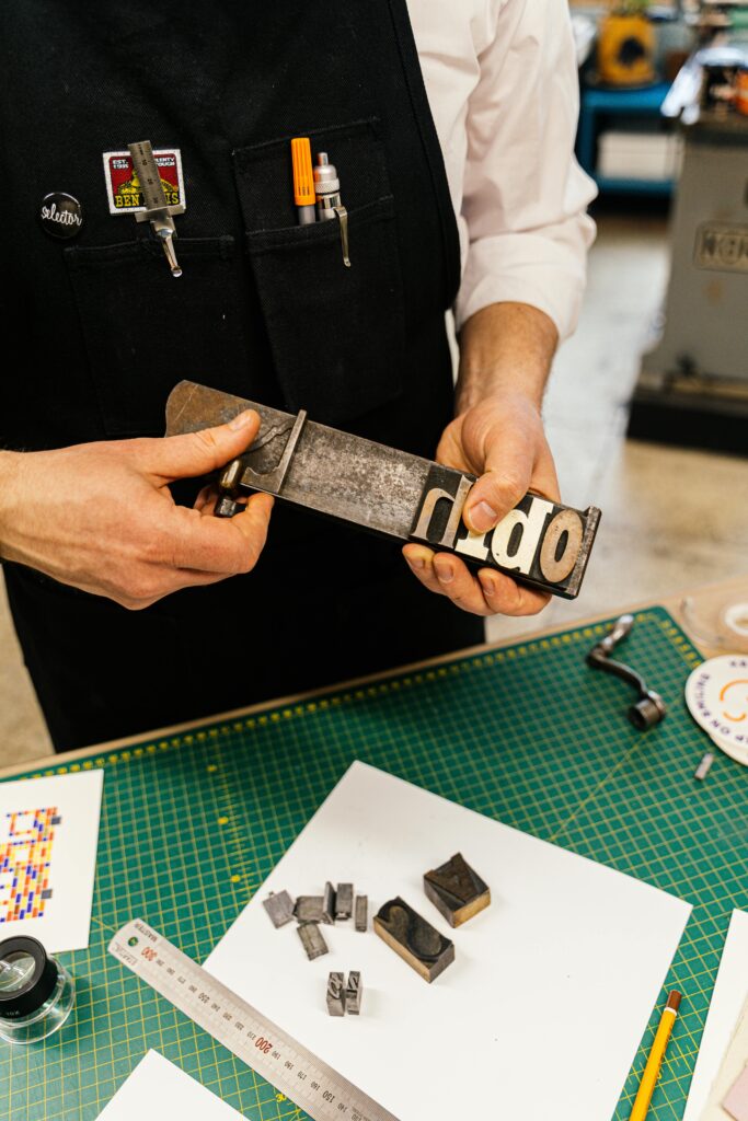 Man in workshop holding a typography block, showcasing craft and design skills.